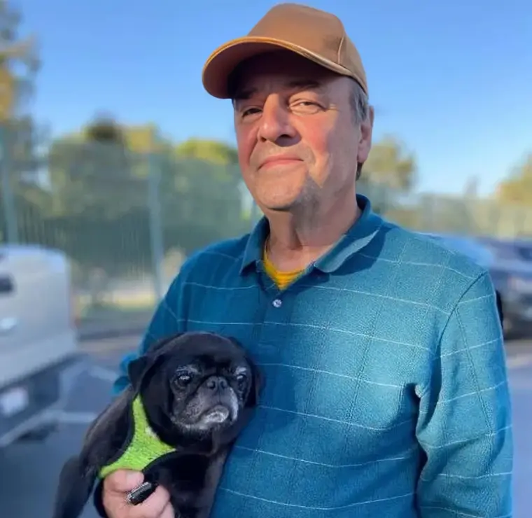 New Project(3) Man holding a small black dog outdoors.